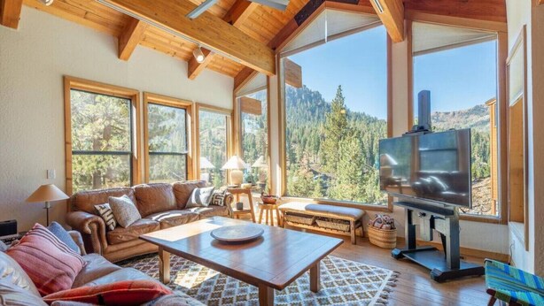 A spacious living room with a large wooden ceiling, a leather sofa, a wooden coffee table, and a television.