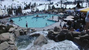 A pool area with multiple swimming pools surrounded by rocks and snow-covered mountains in the background.