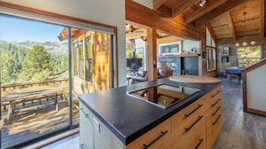 A modern kitchen with a large island, wooden beams, and a view of a mountainous landscape.
