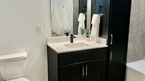 Une salle de bain moderne avec des toilettes blanches, un meuble-lavabo noir doté d’un miroir et un lavabo blanc.