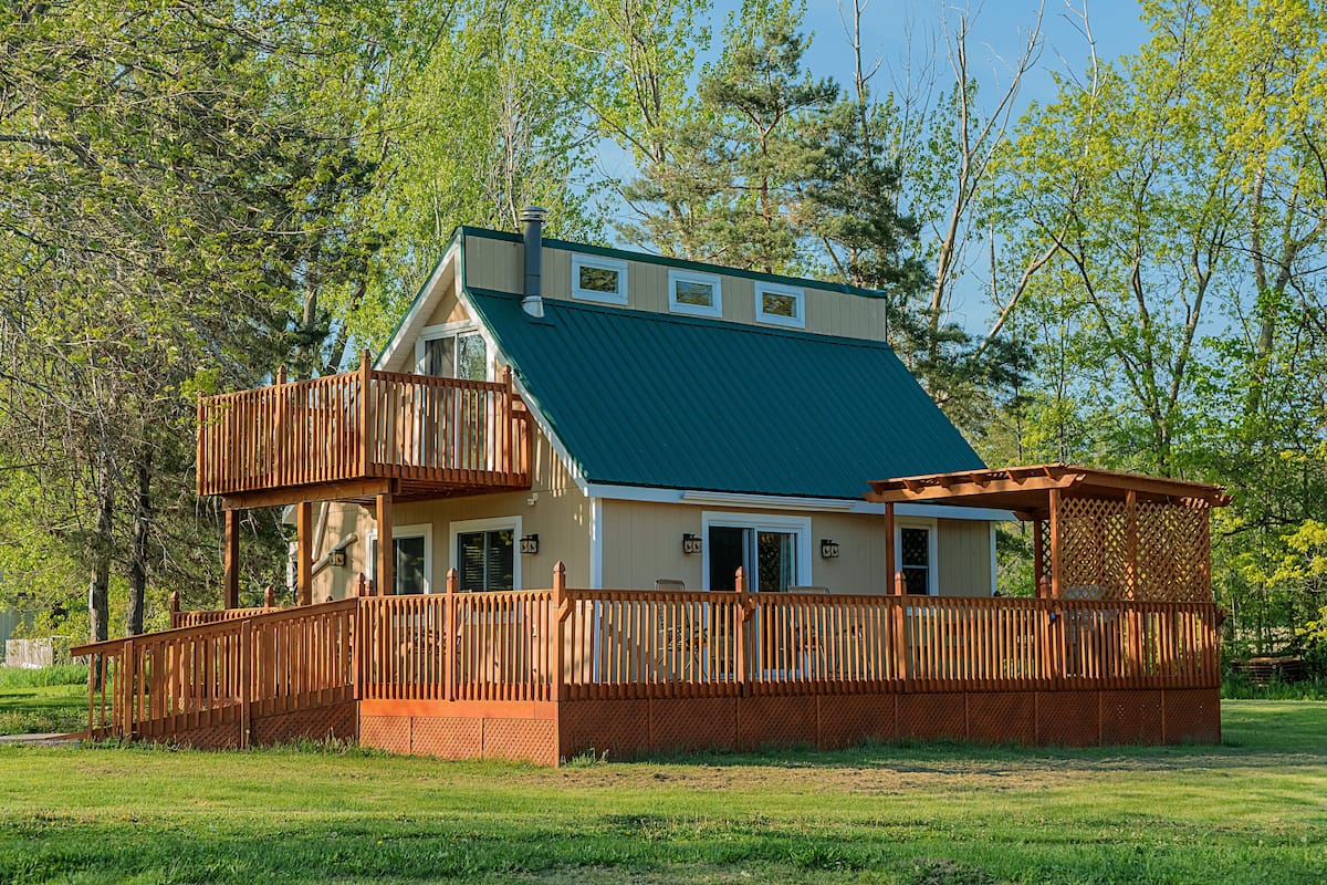 A two-story house with a green roof, a wooden deck, and a fenced outdoor area.
