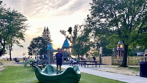 Un parque con un área de juegos, bancos y una llamativa escultura verde.