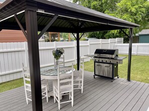 A covered outdoor patio with a grill, white wicker chairs, and a glass table.