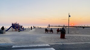 Una playa con un parque infantil, un muelle y un atardecer.