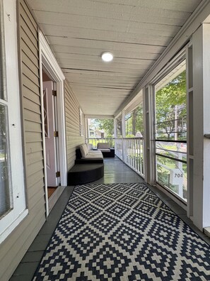 Un porche abrité, agrémenté d’un tapis à motifs, d’un banc et d’une porte donnant sur la maison.