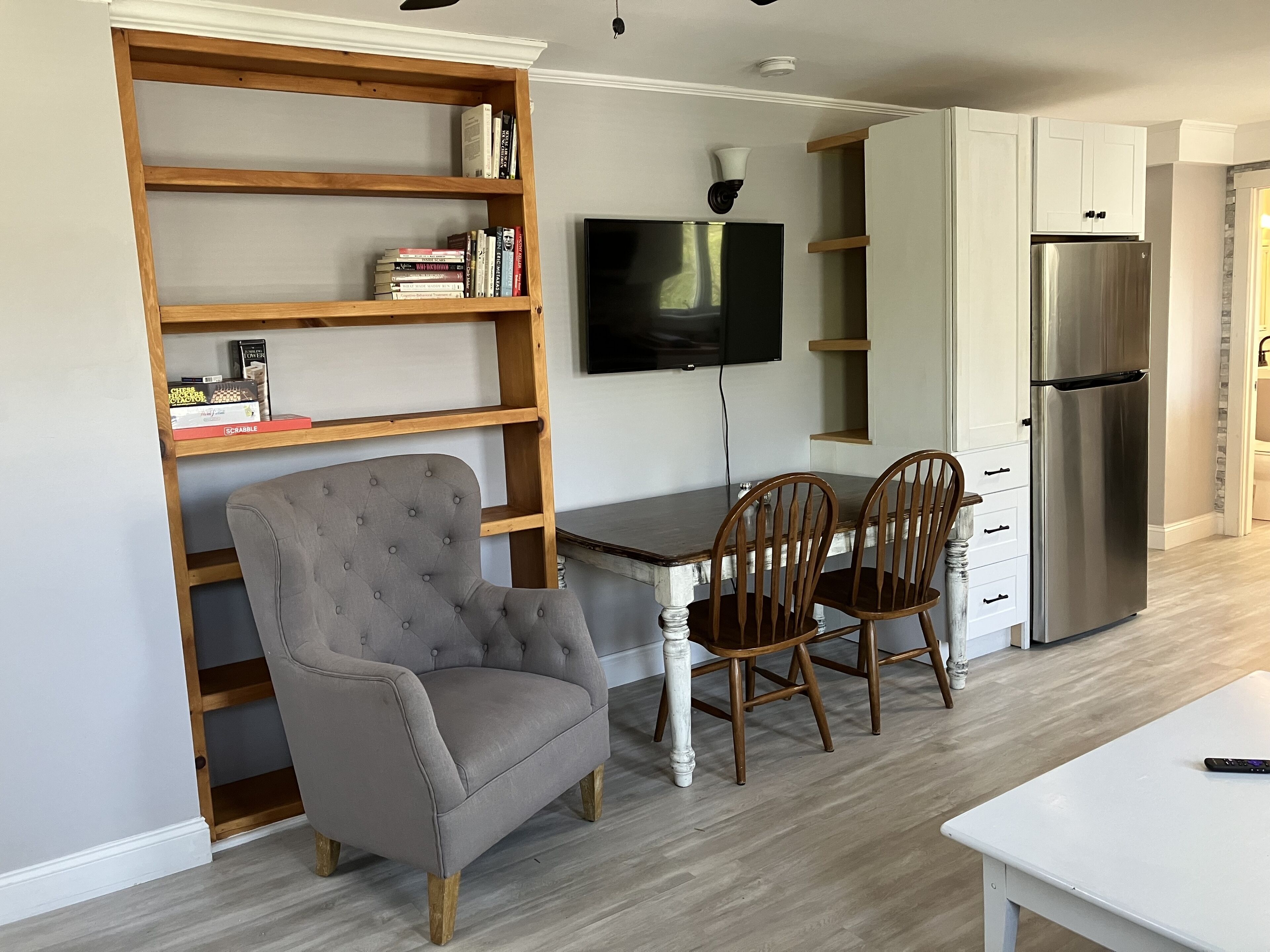 A modern kitchen with a dining area, wooden shelves, a television, and a stainless steel refrigerator.