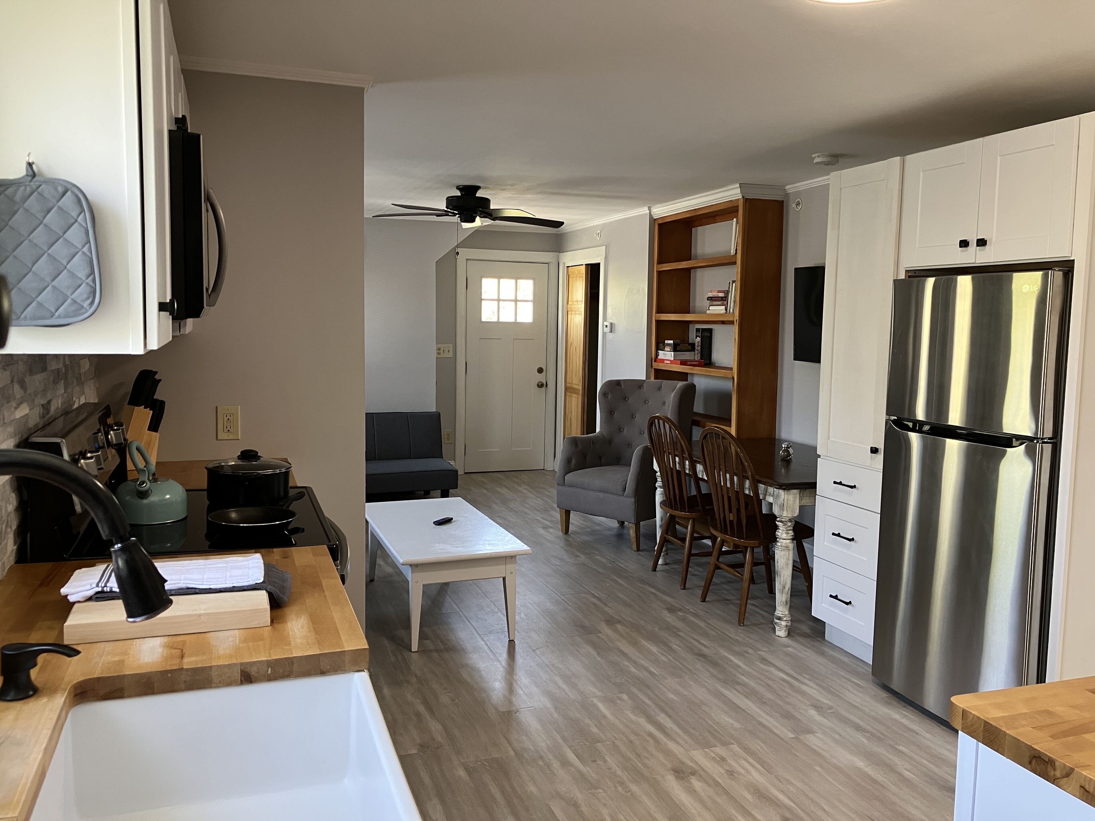 A modern kitchen with a stainless steel refrigerator, wooden cabinets, a dining area with a table and chairs, and a ceiling fan.