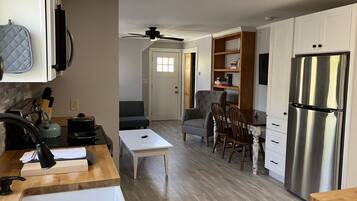 A modern kitchen with a stainless steel refrigerator, wooden cabinets, a dining area with a table and chairs, and a ceiling fan.