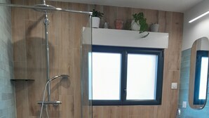 Un baño moderno con cabina de ducha de vidrio, paredes de madera, un ventanal grande y un mueble de tocador de madera con lavabo rojo.