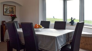 Un coin repas avec une table dressée pour quatre personnes, des chaises, un vase rempli de fleurs et une fenêtre donnant sur la campagne.