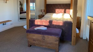 Une chambre à coucher avec un lit à baldaquin, un banc en bois, une table de chevet et un miroir.