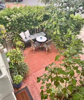 A patio with a round table and chairs, surrounded by potted plants and a small garden area. - Charming Capitol Hill 1BR | Walk to Capitol+Patio (Washington)
