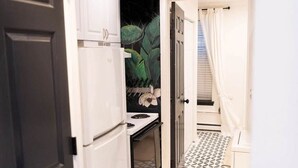 A narrow kitchen with white cabinets, a black door, and a patterned floor.