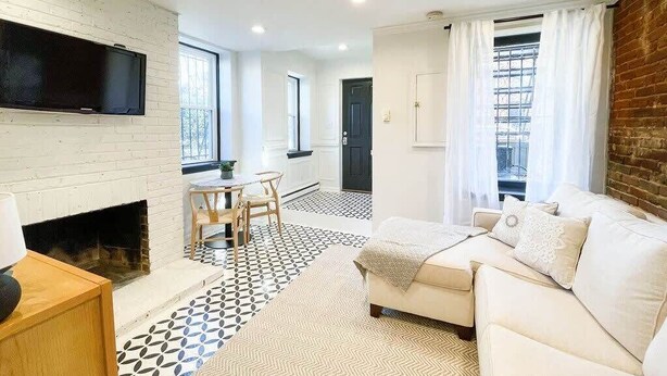 A modern living room with a fireplace, a television mounted on a brick wall, a sofa, and a dining area with a table and chairs.