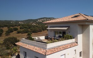 Un bâtiment moderne doté d’un toit en tuiles de terre cuite, d’un balcon avec des meubles d’extérieur et offrant une vue sur un paysage vallonné.