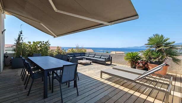 En terrasse med et bord, stole, en sofa og en stor parasol.