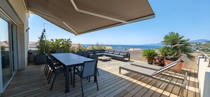 A deck with a table and chairs, a sofa, and a large umbrella. - Appartement Toit Terrasse "villa Ô Perchée" (Albitreccia)