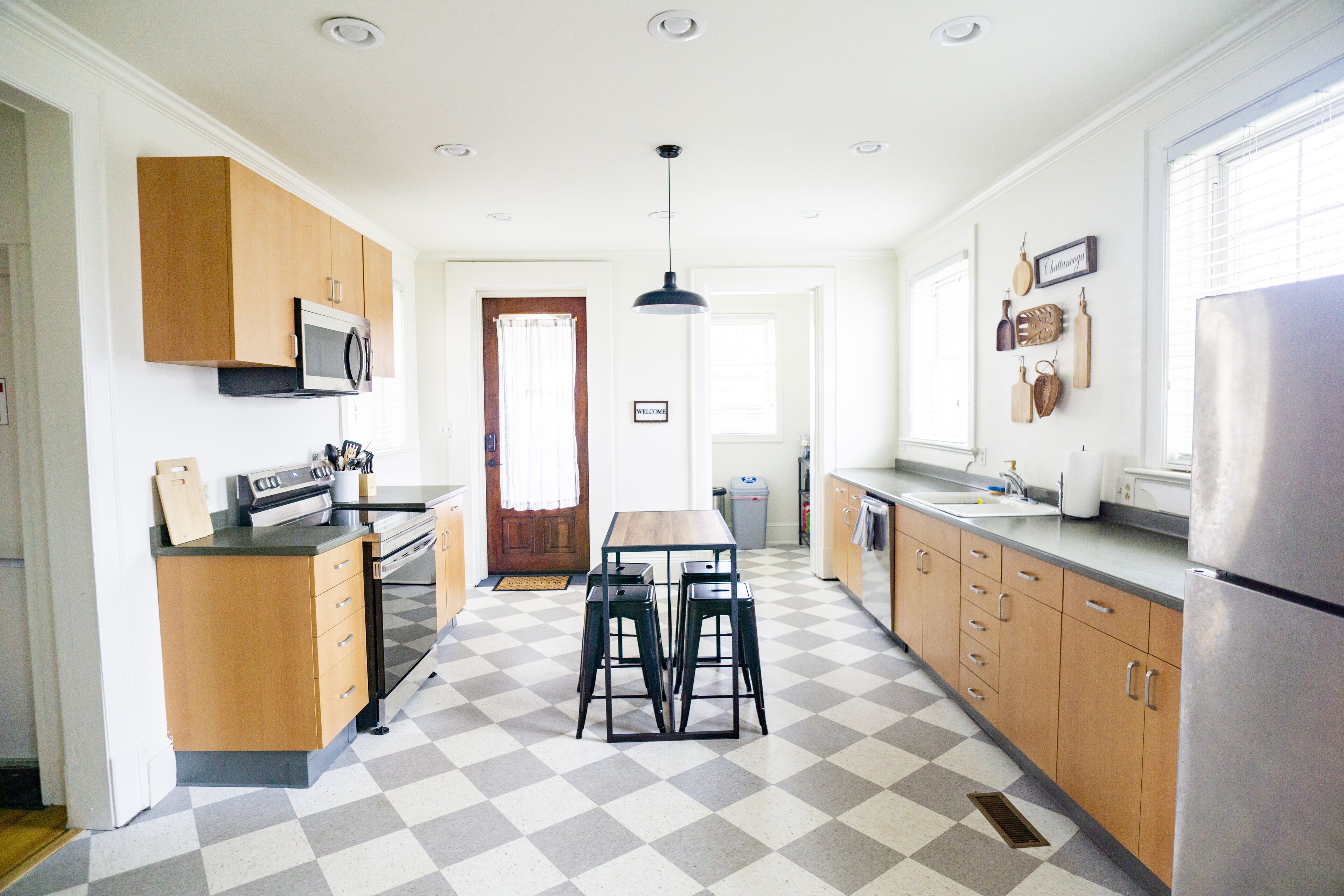 A kitchen with a checkered floor, wooden cabinets, a microwave, a sink, and a refrigerator.