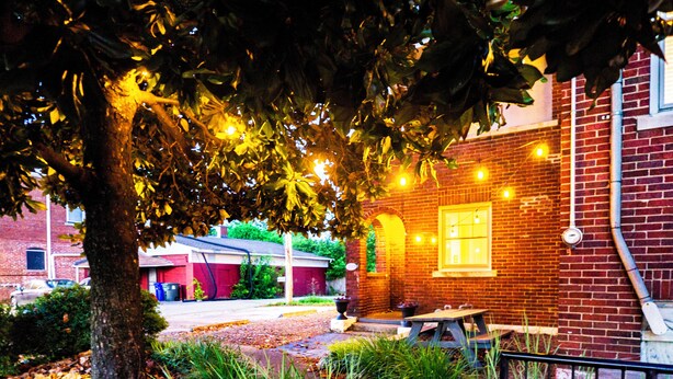 A brick building with a table and chairs outside, surrounded by trees and a fence.