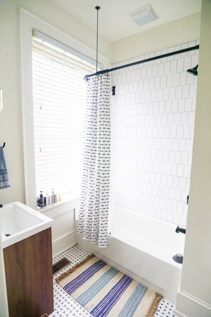 Bathroom features a bathtub, shower curtain, and sink with a wooden cabinet.