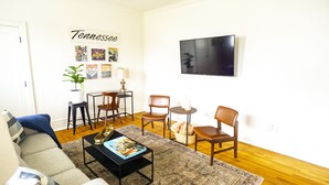 A living room with a sofa, coffee table, chairs, a TV, and wall decorations.