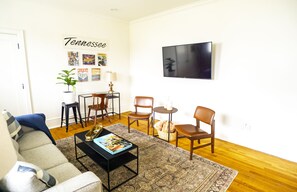 Relax in this inviting living room with a sofa, coffee table, and TV, surrounded by artwork and a potted plant.