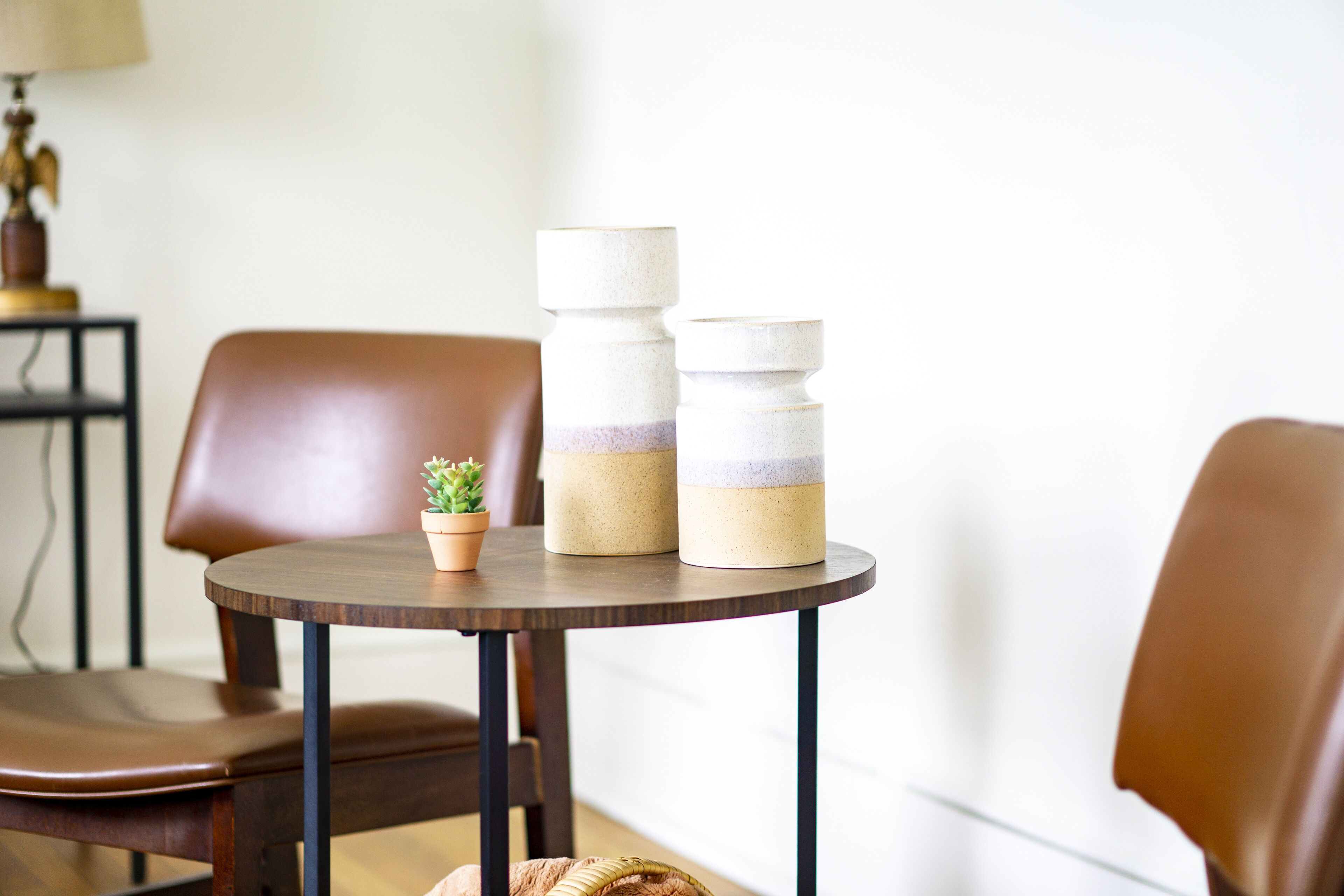Una mesa de madera redonda con dos recipientes de cerámica apilados, una pequeña planta en maceta y una silla de cuero marrón.