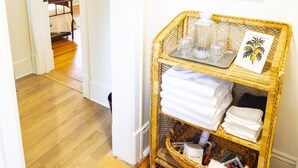 A hallway with a wicker basket containing folded towels and a tray with glasses. There are framed pictures on the wall.