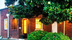 A brick building with a sign reading 'GUESTS' above the door, a small porch, and a well-maintained hedge in front.