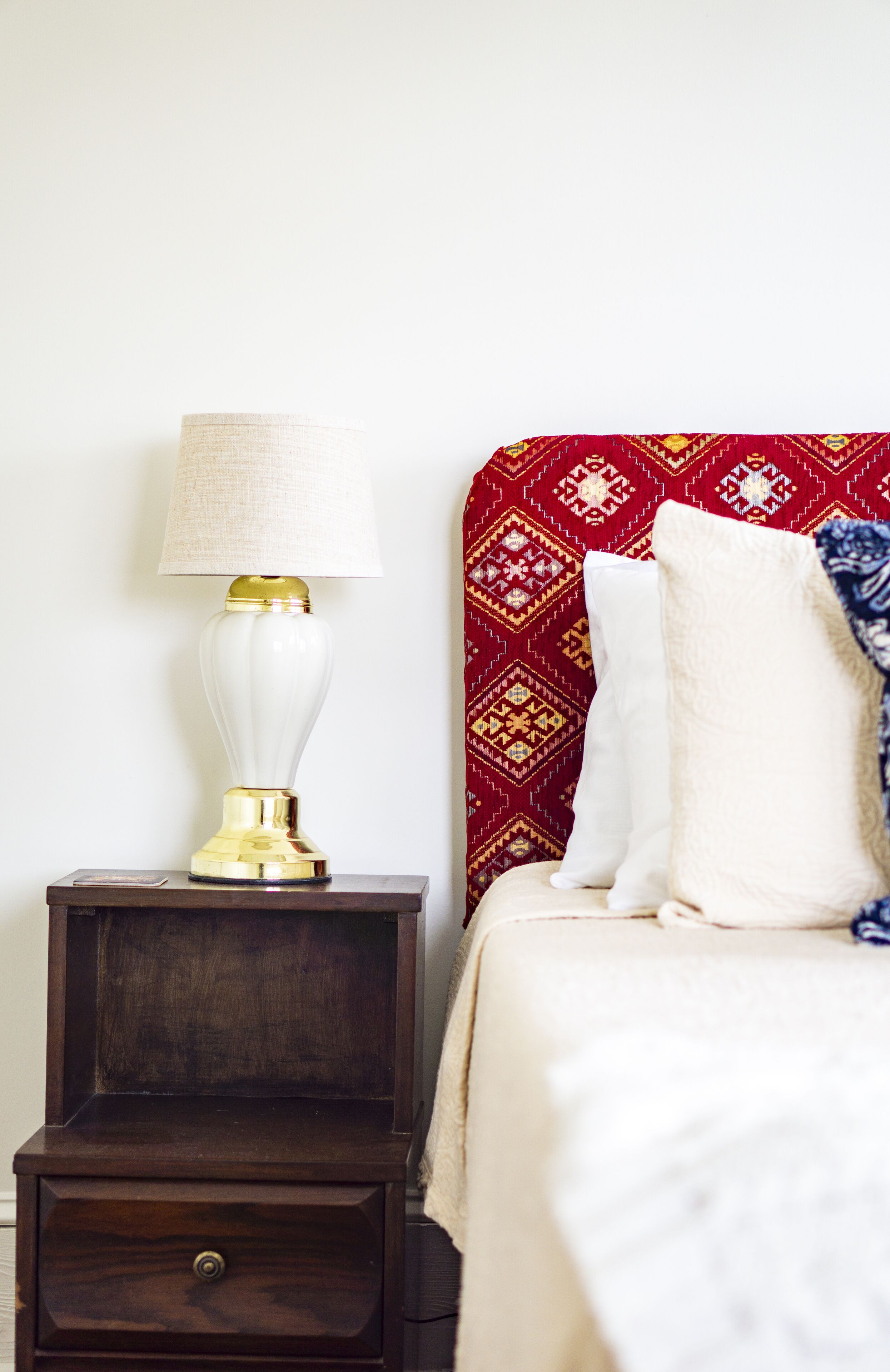 Un lit avec une tête de lit à motifs, une lampe de chevet et une table de chevet dotée d’un tiroir.