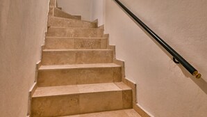 A staircase with beige steps and black handrails, leading upwards in a narrow hallway.