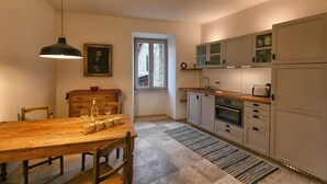A kitchen with a wooden table, chairs, a hanging light, cabinets, a microwave, and a refrigerator.