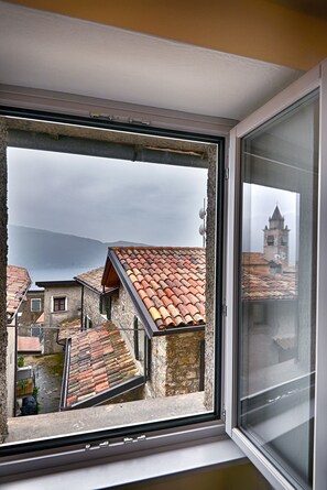 A window with a view of a town's buildings, a church tower, and a body of water.
