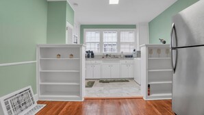 Una cocina con armarios blancos, un refrigerador de acero inoxidable y una ventana con persianas.