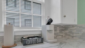 Un baño moderno con encimera de mármol, barra de café y ventana con persianas.