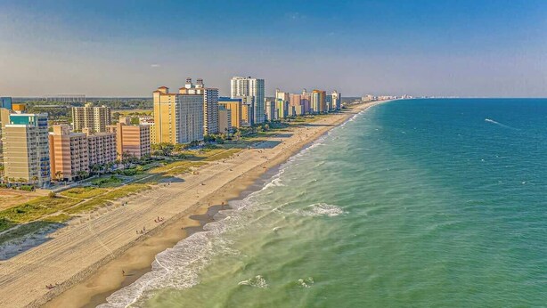 A coastal cityscape with a beachfront, high-rise buildings, and a clear sky. - River Oaks Unit 63C -Near Golf Areas! (Myrtle Beach)