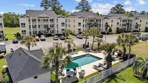 A multi-story hotel with a swimming pool, outdoor seating, and palm trees. - River Oaks Unit 63C -Near Golf Areas! (Myrtle Beach)