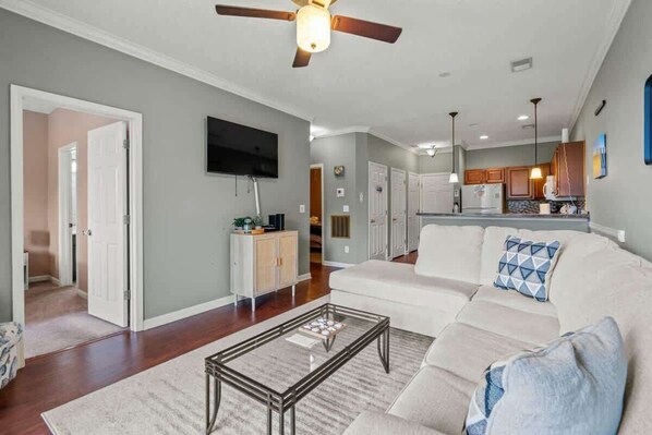 A spacious living room with a large sofa, a coffee table, and a ceiling fan.