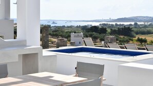 Una terraza en la azotea con piscina, zona de estar y vistas al mar y edificios a lo lejos.