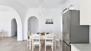 Una cocina moderna con armarios blancos, un refrigerador de acero inoxidable y un comedor con mesa y sillas blancas.