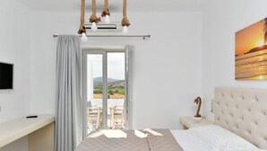 Un dormitorio con cama, escritorio, silla, mesita de noche, televisor y vistas al exterior.