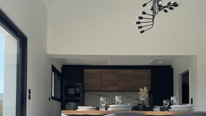 Un'area pranzo moderna con un tavolo lungo, quattro sedie grigie e un lampadario nero.