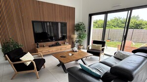 Un soggiorno moderno con una TV a schermo piatto, una parete d'accento in legno, un ampio divano nero, un tavolino da caffè e vista all'esterno.
