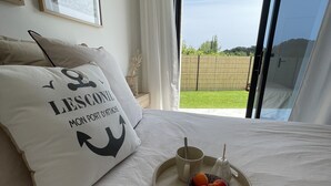 Camera da letto con un letto, cuscini, un vassoio con frutta, una tazza e vista su un paesaggio verde attraverso una porta scorrevole.