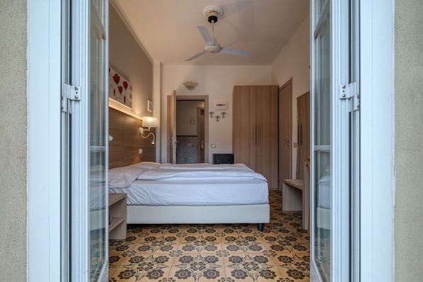 Un dormitorio con una cama, ventilador de techo, puerta y suelo estampado.