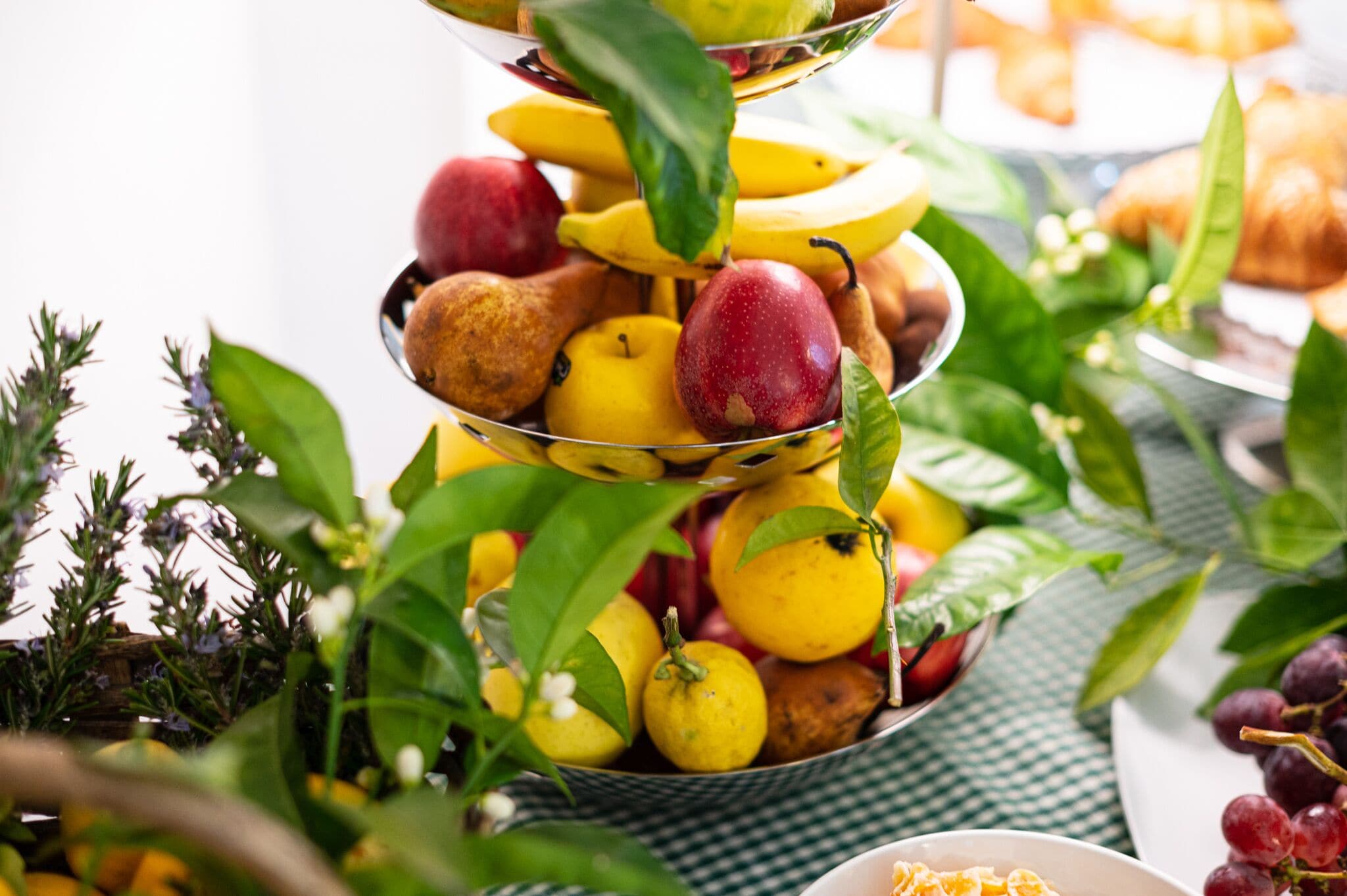 A tiered fruit stand with apples, bananas, and pears, surrounded by greenery.