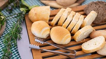 Various types of bread on a wooden cutting board with a knife and bread slicer.