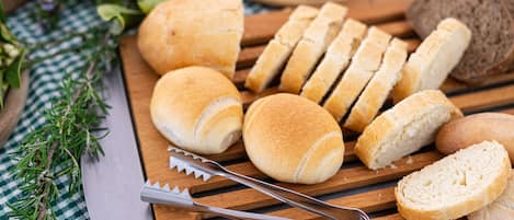 Various types of bread on a wooden cutting board with a knife and bread slicer.