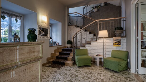 A spacious living area with a staircase, a green armchair, a wooden cabinet, and a patterned floor. - Hotel Vecchie Mura  (Finale Ligure)