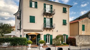 A two-story building with green shutters, a balcony on the second floor, and a small garden area in front. - Hotel Vecchie Mura  (Finale Ligure)